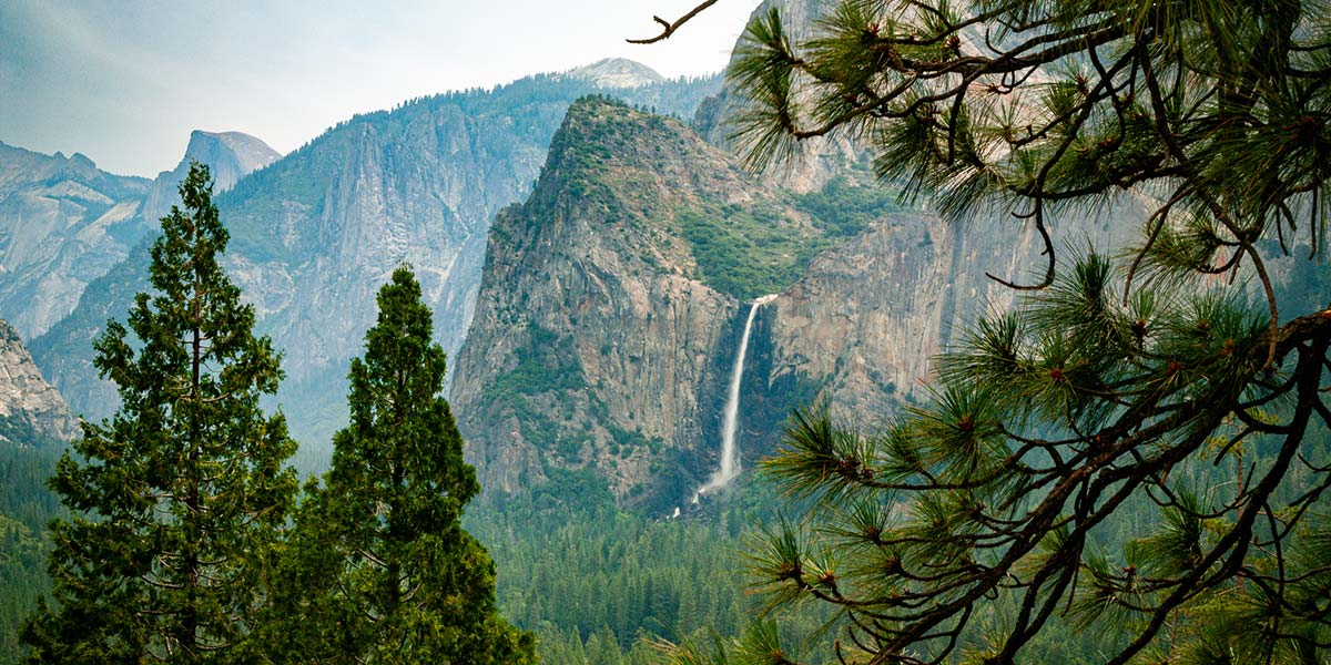 A scenic view of a waterfall cascading down a cliff surrounded by towering trees and mountains.