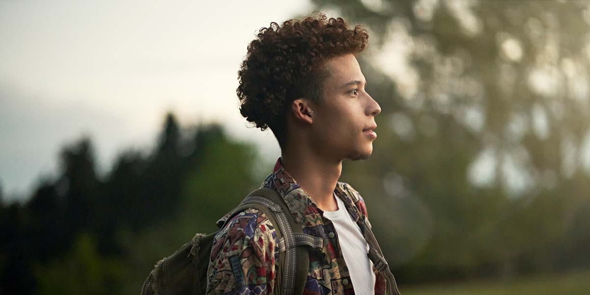A man outdoors with a thoughtful expression, carrying a backpack and looking into the distance.