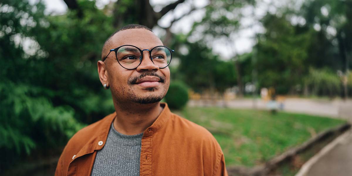 A man with glasses and a warm smile, standing outside in a green park.